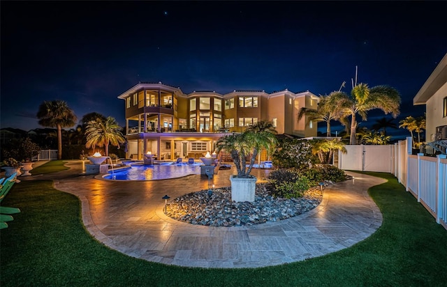 back house at night featuring a balcony, a yard, a fenced in pool, and a patio