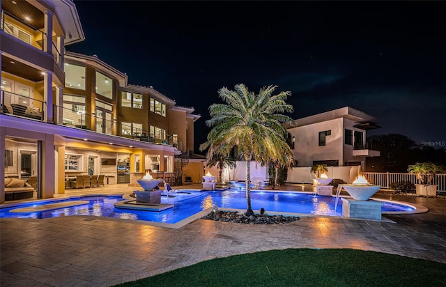 pool at night featuring a patio, pool water feature, area for grilling, and an in ground hot tub