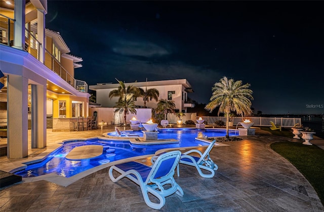 pool at night featuring an in ground hot tub, a patio, and exterior bar