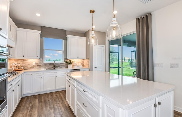 kitchen with sink, tasteful backsplash, a center island, hanging light fixtures, and white cabinets