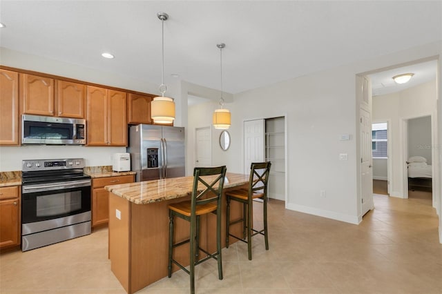 kitchen featuring light stone counters, stainless steel appliances, a kitchen island, a kitchen bar, and decorative light fixtures