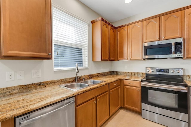 kitchen featuring light tile patterned floors, light stone counters, stainless steel appliances, a sink, and brown cabinetry