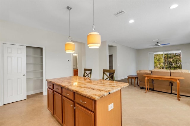 kitchen featuring light stone counters, recessed lighting, a kitchen island, brown cabinets, and pendant lighting