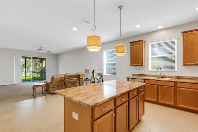 kitchen featuring visible vents, a kitchen island, hanging light fixtures, light stone countertops, and a sink