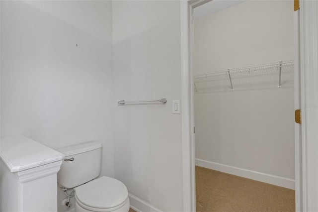 bathroom featuring a walk in closet, toilet, and baseboards