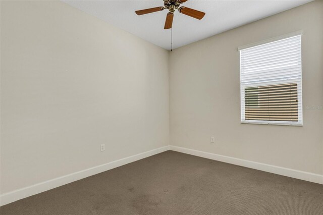 empty room with a ceiling fan, dark carpet, and baseboards