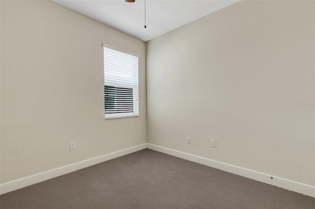 spare room featuring a ceiling fan, dark colored carpet, and baseboards