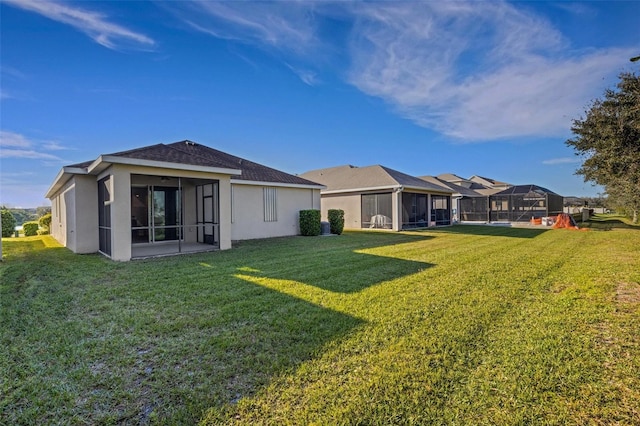 back of property featuring a lawn, a sunroom, and stucco siding