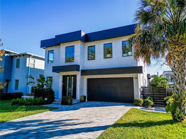 modern home featuring stucco siding, decorative driveway, a garage, and fence