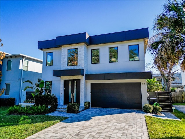 modern home with decorative driveway, fence, an attached garage, and stucco siding