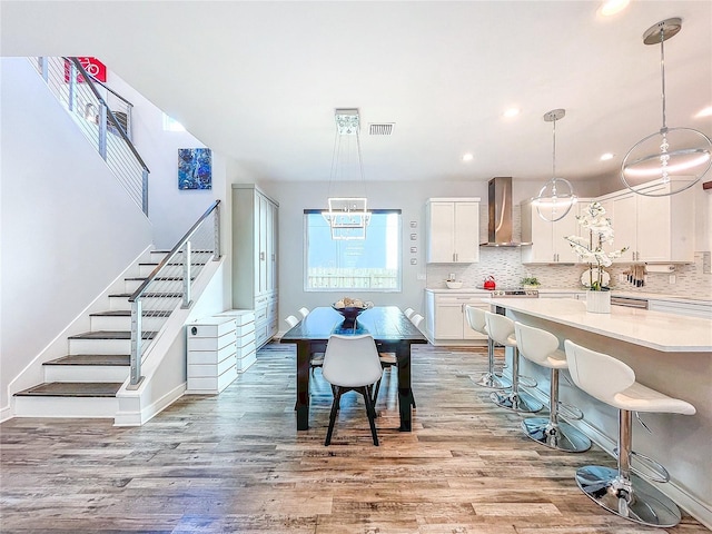 kitchen featuring pendant lighting, wall chimney range hood, light hardwood / wood-style flooring, a breakfast bar area, and white cabinets