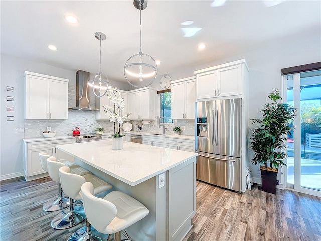 kitchen with a breakfast bar, a sink, stainless steel appliances, light wood-style floors, and wall chimney exhaust hood