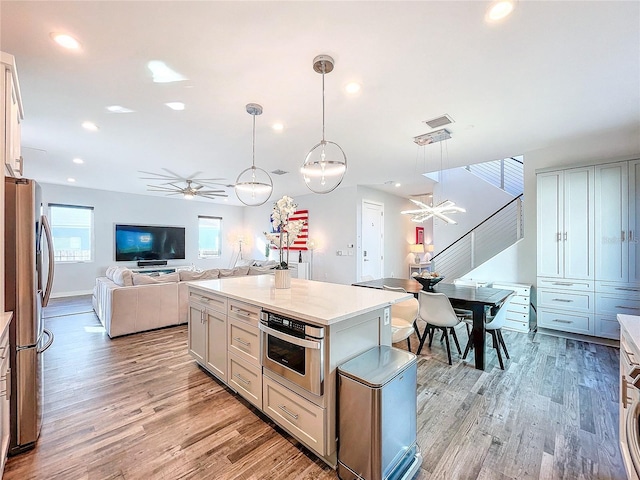 kitchen with light wood-type flooring, open floor plan, stainless steel appliances, light countertops, and hanging light fixtures