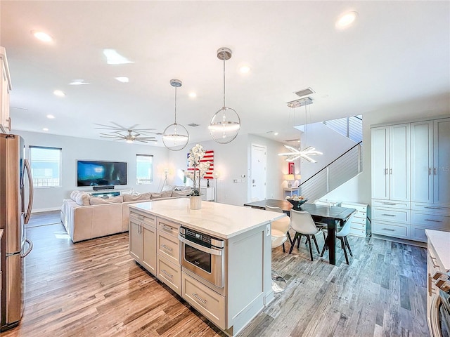 kitchen with stainless steel appliances, white cabinets, a kitchen island, decorative light fixtures, and light wood-type flooring