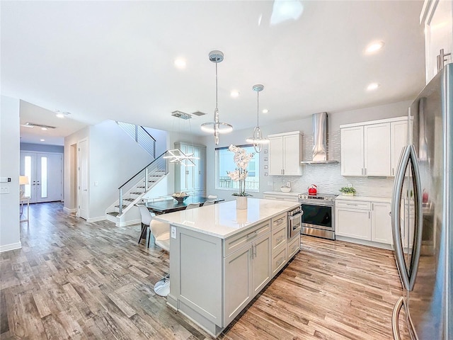 kitchen with decorative light fixtures, white cabinetry, a center island, stainless steel appliances, and wall chimney exhaust hood