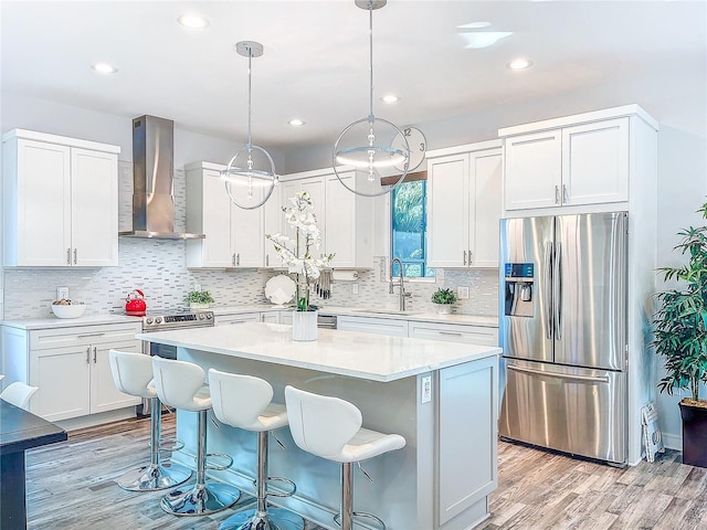 kitchen with wall chimney exhaust hood, sink, a center island, hanging light fixtures, and appliances with stainless steel finishes