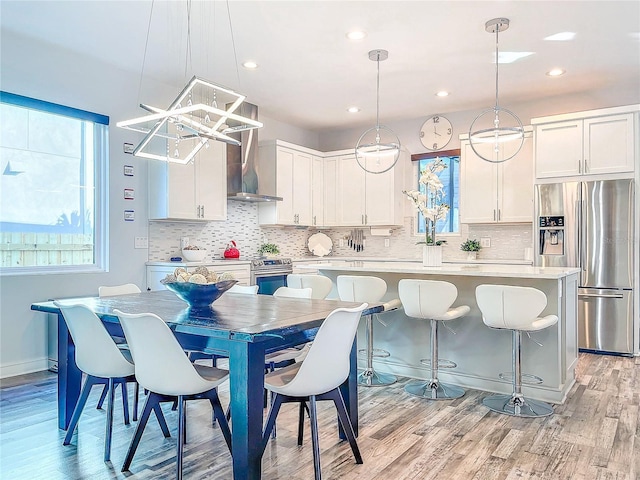 kitchen featuring light wood-style flooring, a kitchen island, stainless steel appliances, wall chimney exhaust hood, and light countertops