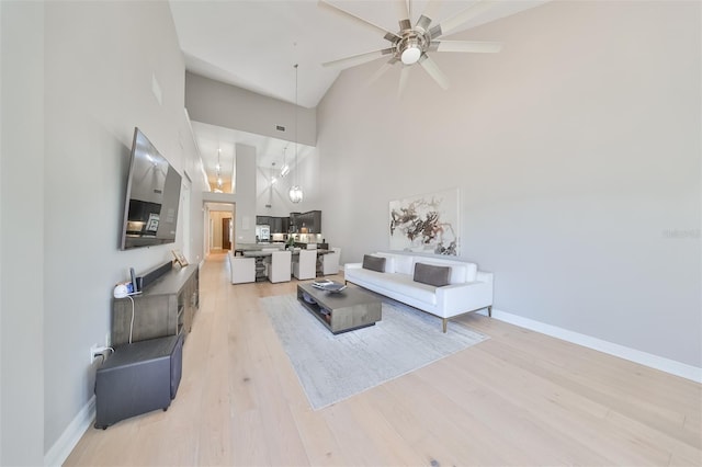 living room featuring ceiling fan, a towering ceiling, and light wood-type flooring