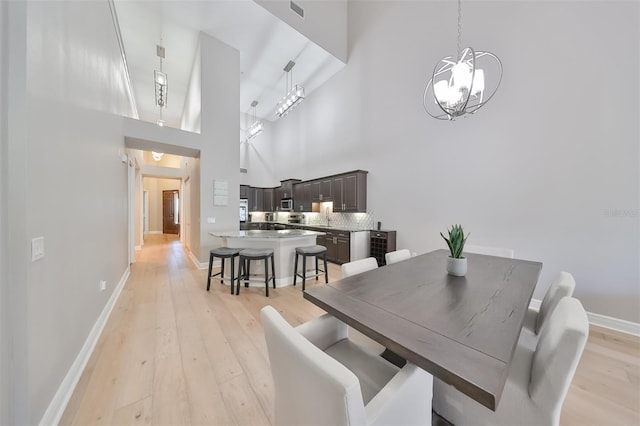 dining area with a towering ceiling, a notable chandelier, and light wood-type flooring