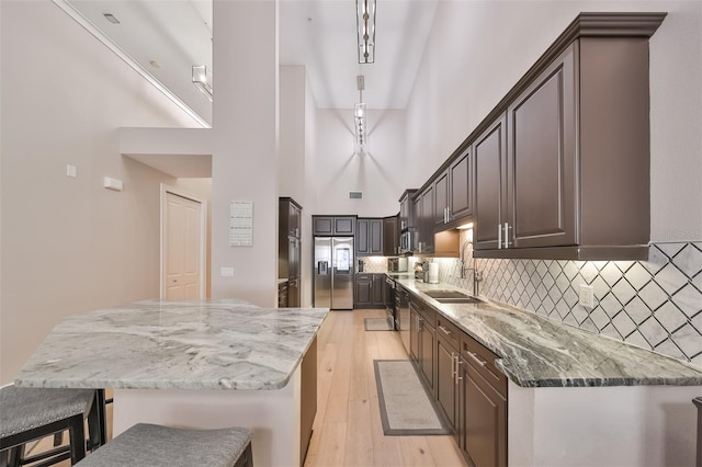 kitchen with a breakfast bar, sink, stainless steel fridge, light hardwood / wood-style floors, and light stone countertops