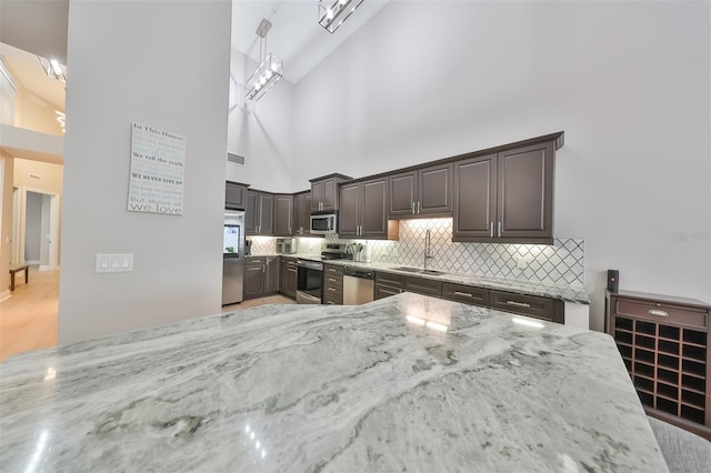 kitchen featuring dark brown cabinetry, sink, high vaulted ceiling, stainless steel appliances, and light stone countertops