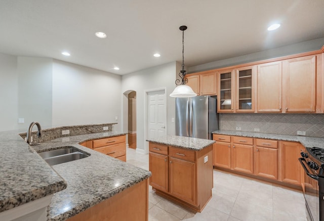 kitchen with gas stove, sink, a center island, hanging light fixtures, and stainless steel fridge