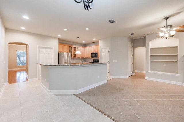 kitchen with light tile patterned flooring, light brown cabinetry, stainless steel fridge, light stone counters, and built in shelves