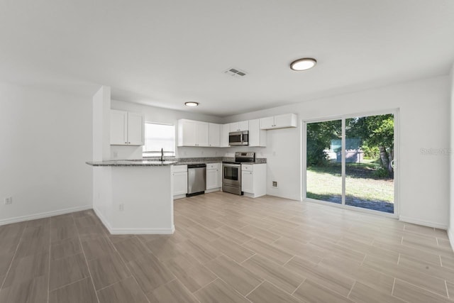 kitchen featuring stainless steel appliances, plenty of natural light, stone countertops, and white cabinets