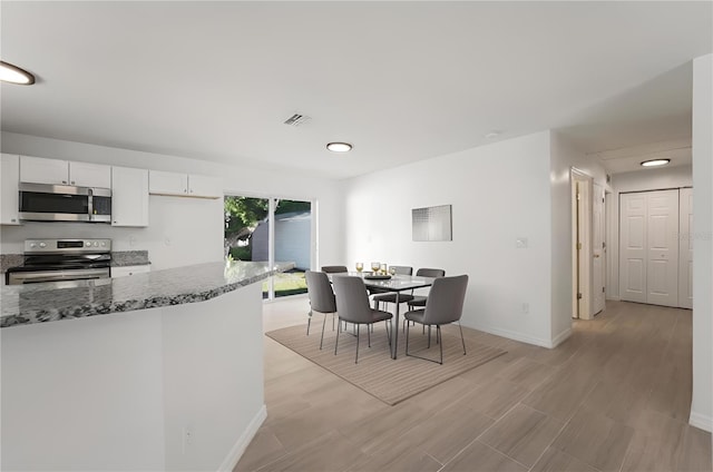 kitchen featuring white cabinetry, stainless steel appliances, and dark stone counters