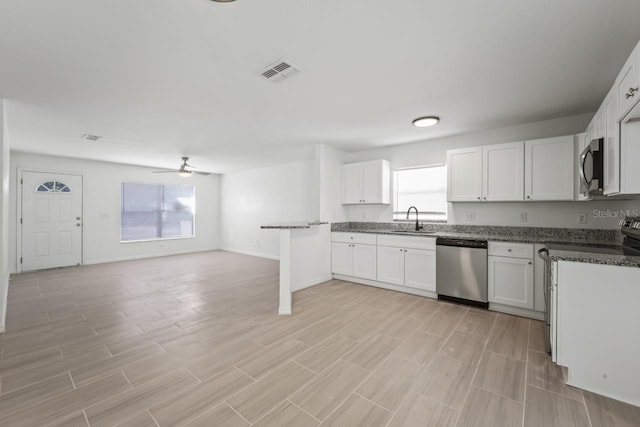 kitchen with sink, appliances with stainless steel finishes, dark stone countertops, a healthy amount of sunlight, and white cabinets