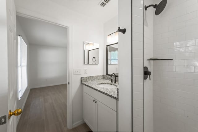 bathroom with vanity, a wealth of natural light, wood-type flooring, and a tile shower