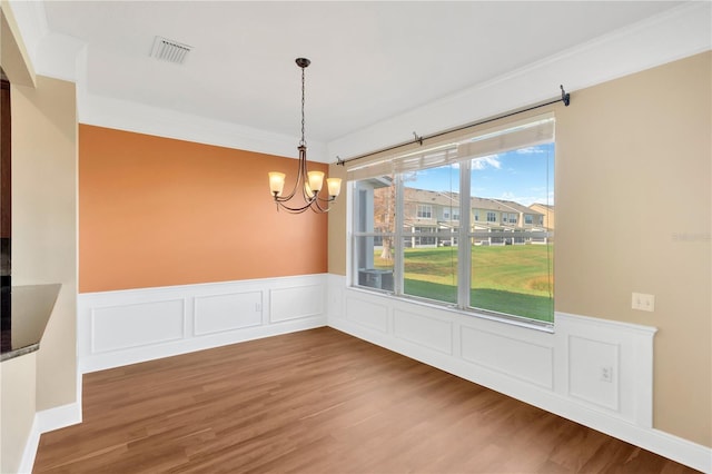 unfurnished dining area with hardwood / wood-style flooring, ornamental molding, and an inviting chandelier