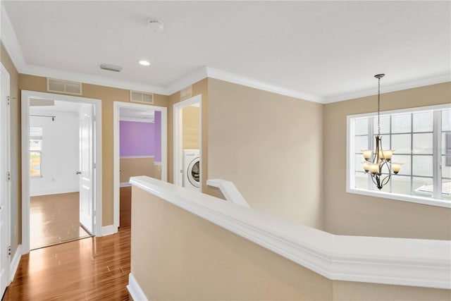 hallway with crown molding, wood-type flooring, washer / dryer, and a notable chandelier