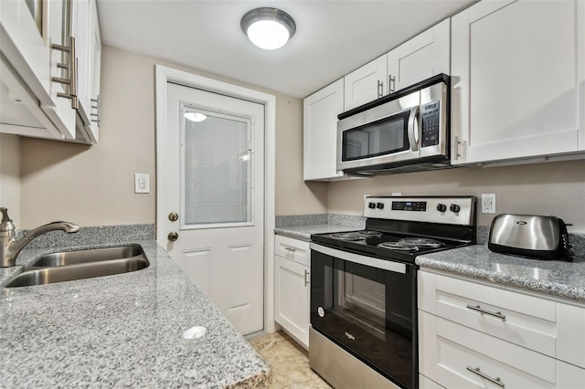 kitchen featuring appliances with stainless steel finishes, white cabinetry, sink, light tile patterned floors, and light stone countertops