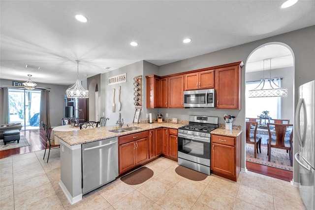 kitchen featuring stainless steel appliances, sink, light stone counters, and decorative light fixtures