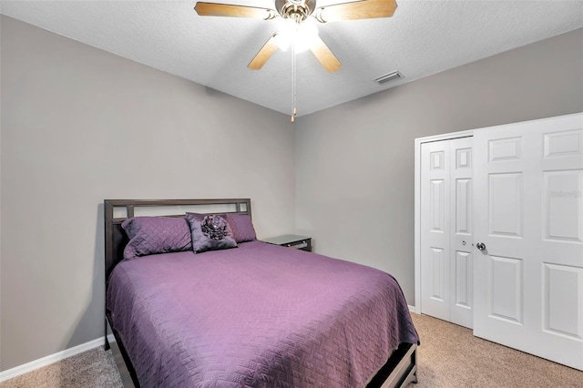 bedroom with ceiling fan, light colored carpet, a closet, and a textured ceiling