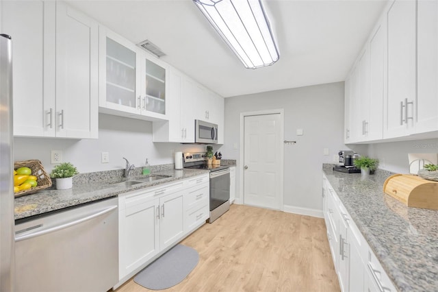 kitchen featuring sink, appliances with stainless steel finishes, white cabinetry, light stone countertops, and light wood-type flooring