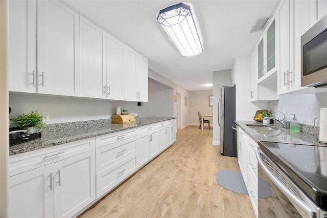 kitchen with white cabinetry, sink, light stone counters, stainless steel appliances, and light hardwood / wood-style flooring