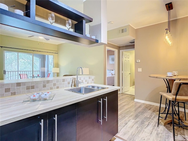 kitchen featuring sink, light stone counters, hanging light fixtures, light hardwood / wood-style flooring, and decorative backsplash