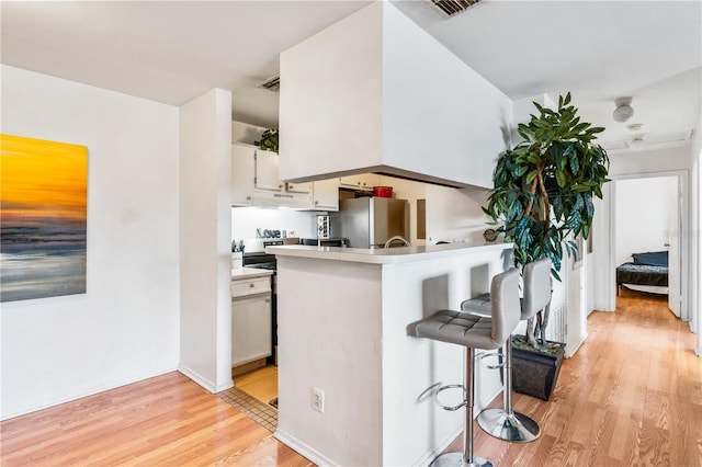 kitchen featuring stainless steel fridge, white cabinets, a kitchen bar, kitchen peninsula, and light hardwood / wood-style flooring