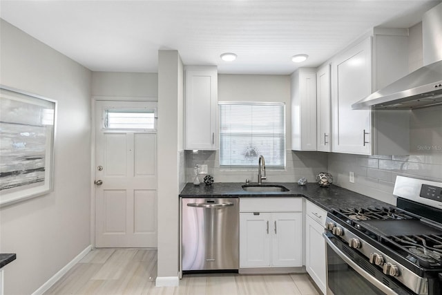 kitchen featuring appliances with stainless steel finishes, a sink, wall chimney range hood, white cabinetry, and backsplash