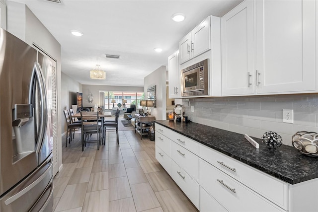 kitchen featuring white cabinetry, open floor plan, appliances with stainless steel finishes, tasteful backsplash, and dark stone countertops