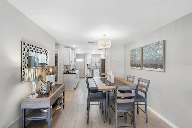 dining area featuring light wood-style flooring, visible vents, a textured ceiling, and baseboards