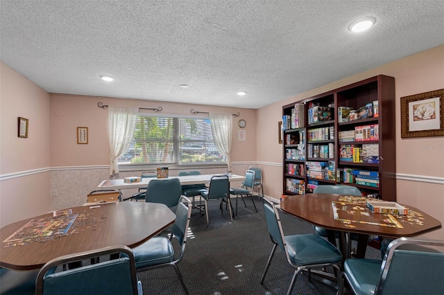 carpeted dining space with a textured ceiling and wainscoting