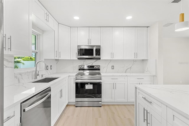 kitchen with sink, appliances with stainless steel finishes, light stone counters, white cabinets, and decorative light fixtures