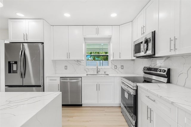 kitchen with stainless steel appliances, white cabinetry, sink, and light stone counters