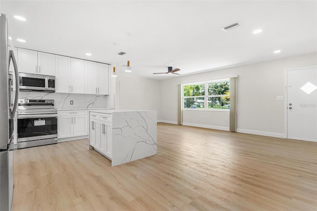 kitchen with decorative light fixtures, tasteful backsplash, white cabinets, stainless steel appliances, and light wood-type flooring