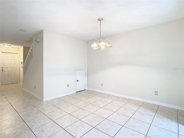 tiled spare room with a notable chandelier