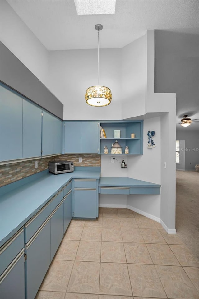 kitchen with a skylight, blue cabinets, backsplash, hanging light fixtures, and light tile patterned floors