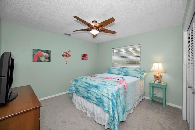 bedroom featuring a textured ceiling, light colored carpet, a closet, and ceiling fan